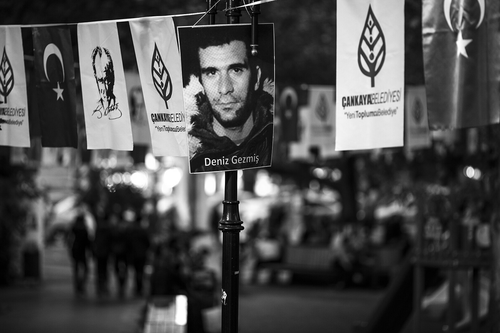 Fotografie eines jungen Mannes an einem Laternenpfahl, daneben andere politische Plakate