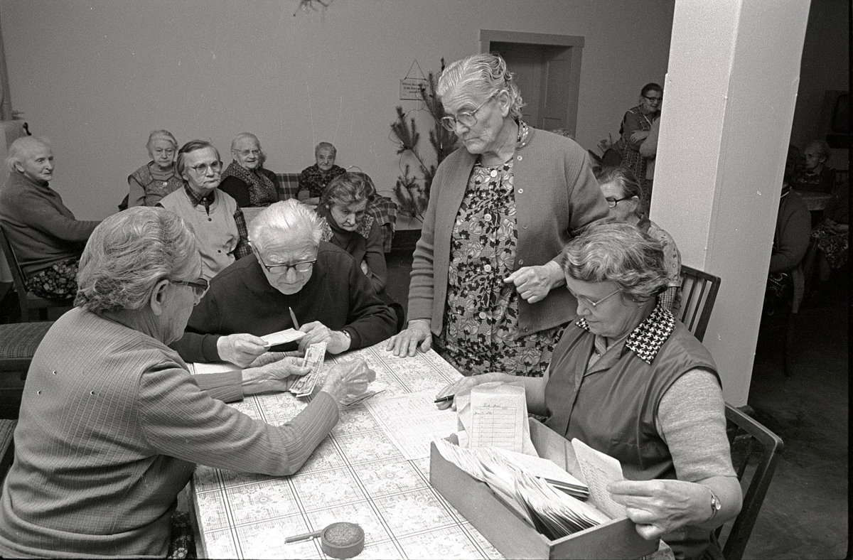 Eine Gruppe von älteren Leuten sitzt an einem Tisch, an dem Geld ausgezahlt wird.