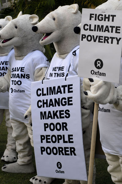 Foto mehrere Menschen in Eisbärkostümen. Ein Schild im Vordergrund mit der Aufschrift: climat change makes poor people poorer, oxfam.