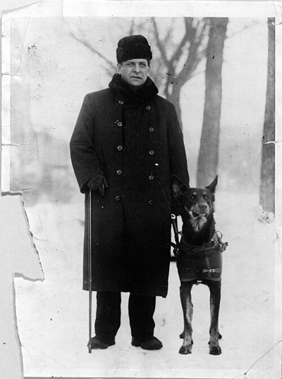 Schwarzweißfoto eines Mannes mit Hund im Geschirr in einer Schneelandschaft