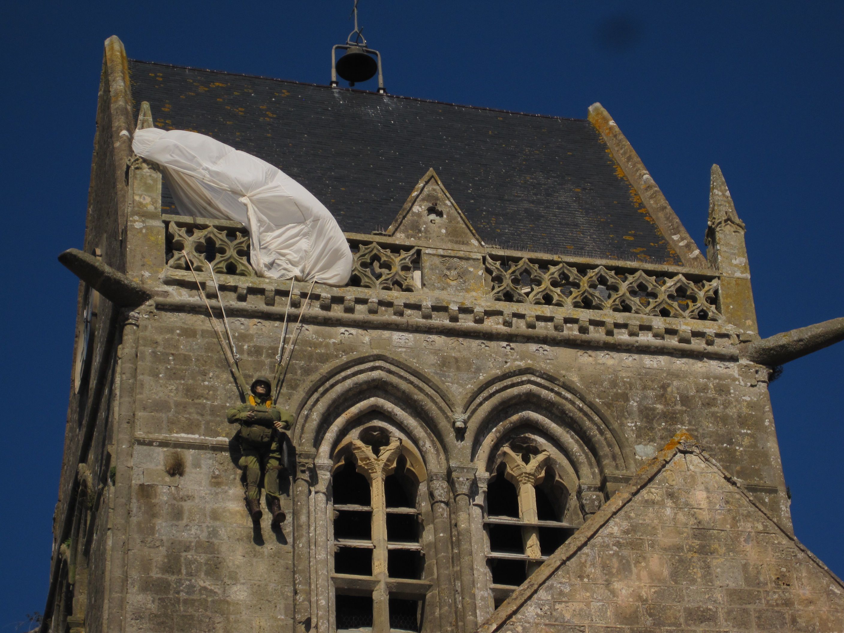 Another form of the public representation of history is the paratrooper effigy on the steeple of the church of Sainte-Mère-Église in Normandy, France. It commemorates an American soldier who accidentally got caught on the church spire during the D-Day invasion of 1944. This playful monument shows a relatively casual approach to history, the effigy seeming almost like an advertisement for the Airborne Museum located across from the church. Photo: Irmgard Zündorf, Sainte-Mère-Église 2015, License [https://creativecommons.org/licenses/by-nc/3.0/de/ CC BY-NC 3.0 DE]