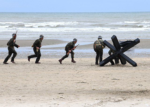 U.S. Navy troops reenacting the D-Day invasion in Normandy on the 75th anniversary of the event. Photo: Michael McNabb, June 7, 2019. Source: Commander, U.S. Naval Forces Europe-Africa/U.S. 6th Fleet / [https://www.flickr.com/photos/94966166@N02/48023249368 Flickr] public domain