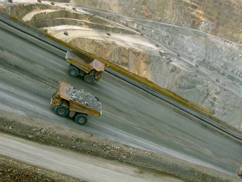 Two loading trucks driving on a road, with a quarry visible in the background.